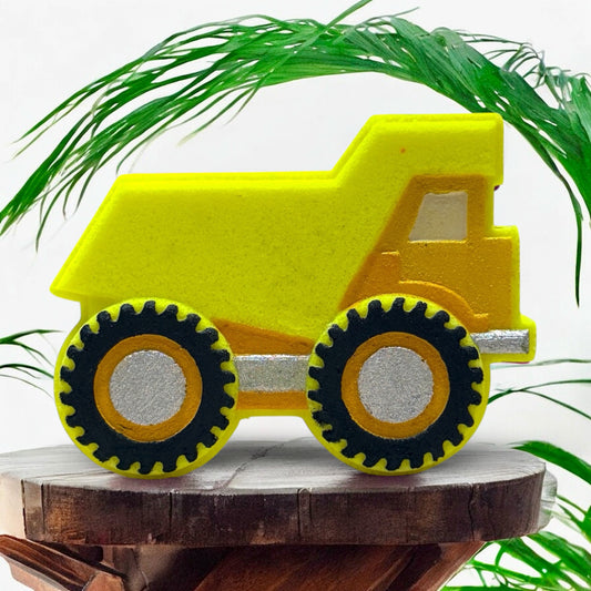 Yellow bath bomb dump truck on a wooden block with green leaves in the background