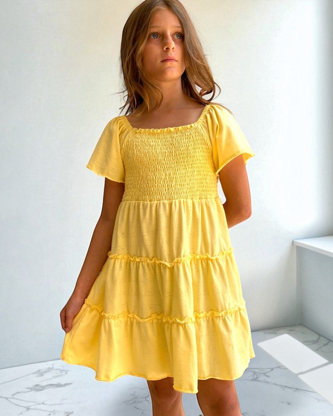 Young girl wearing a yellow dress against a white wall.