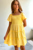 Young girl wearing a yellow dress against a white wall.