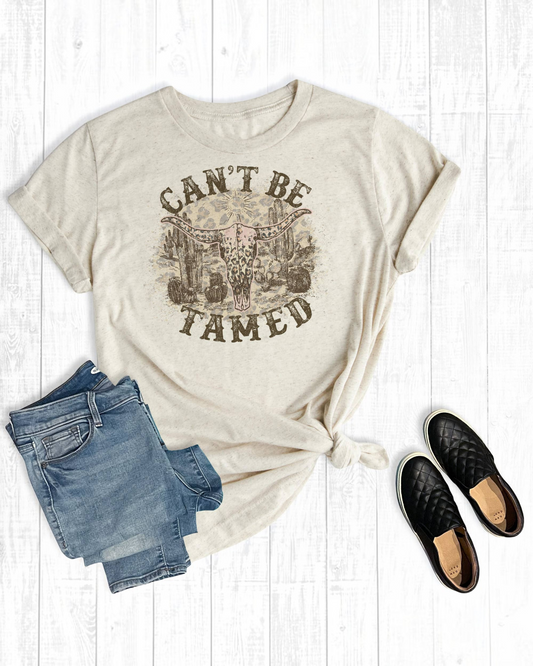 Beige t-shirt with graphic design, denim shorts, and black shoes on a light wooden surface