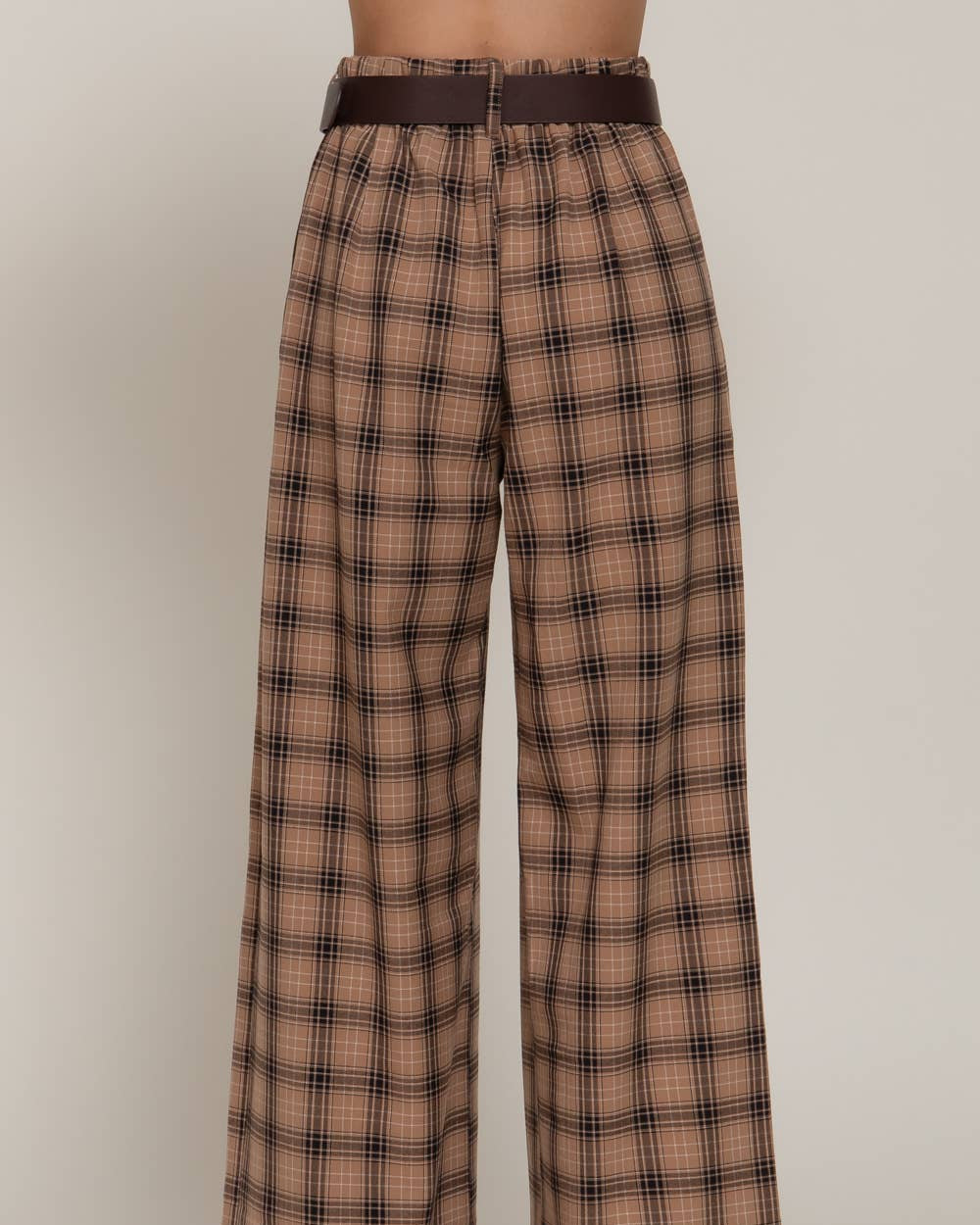 A pair of high-waisted, wide-leg trousers in a brown and beige plaid pattern, featuring a matching dark brown belt, shown on a model from the waist down against a neutral studio background.