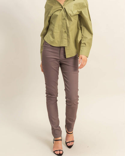 A woman modeling a sage green button-down shirt and taupe slim-fit pants with black high-heeled sandals, standing against a plain light beige studio background.