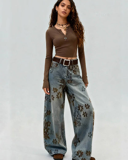 Woman wearing a brown long-sleeve top and floral jeans on a plain background
