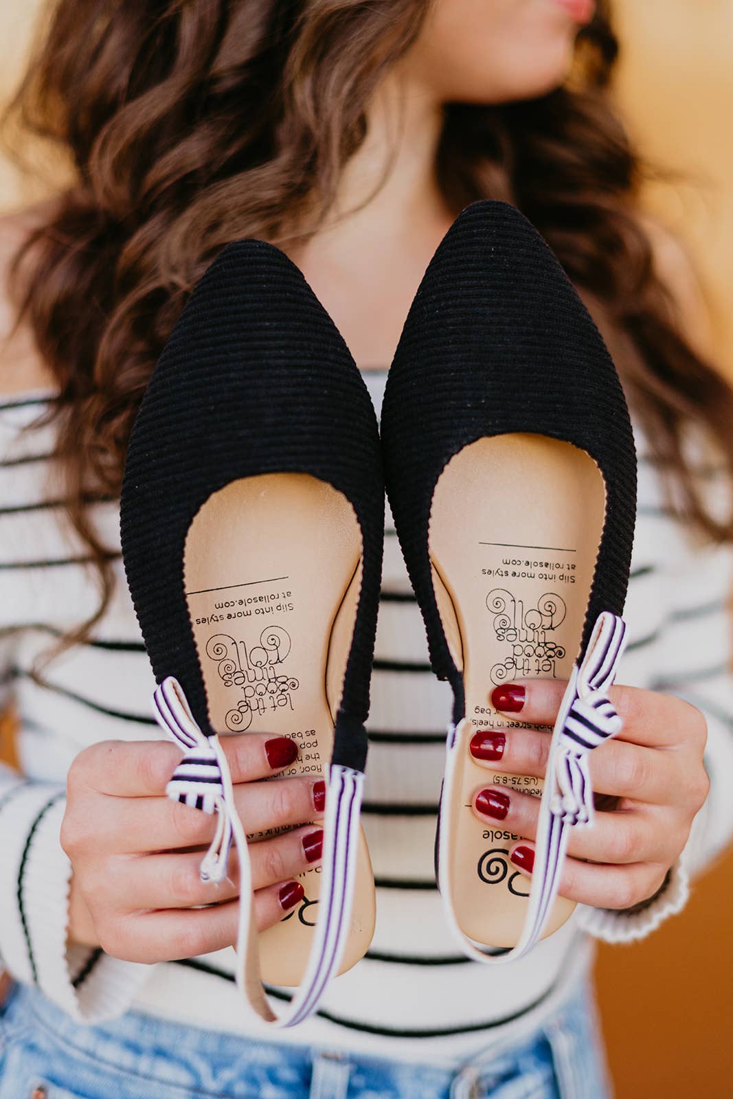 Black flats with decorative bows held by a person wearing a striped shirt.