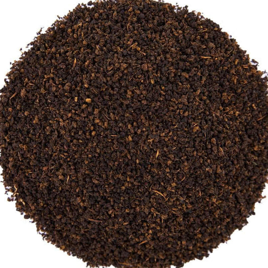 A circular pile of dark brown coffee grounds or tea leaves on a solid white background.