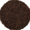 A circular pile of dark brown coffee grounds or tea leaves on a solid white background.