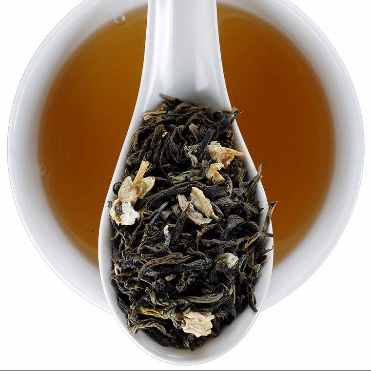 A white ceramic cup filled with amber tea, with a white spoon resting inside the cup and holding loose-leaf jasmine tea. The Elmwood Texas Inn logo is visible in the top right corner.