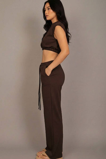 Woman wearing a brown sleeveless top and wide-leg pants against a plain background