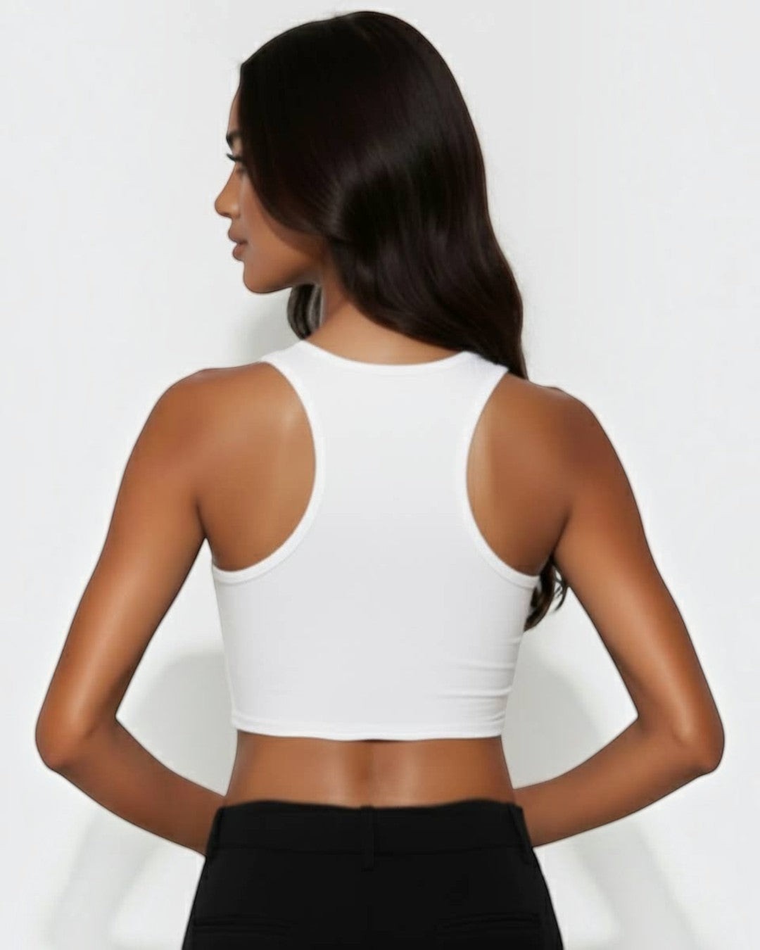 Woman wearing a white crop top and black pants on a plain background