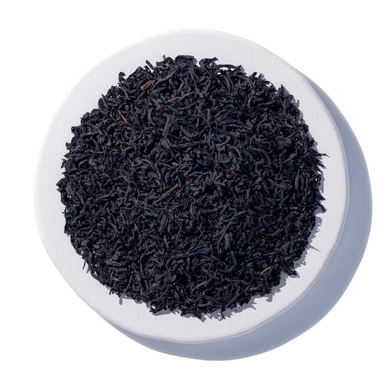 A top-down view of loose-leaf tea leaves piled in the center of a round white plate against a white background.