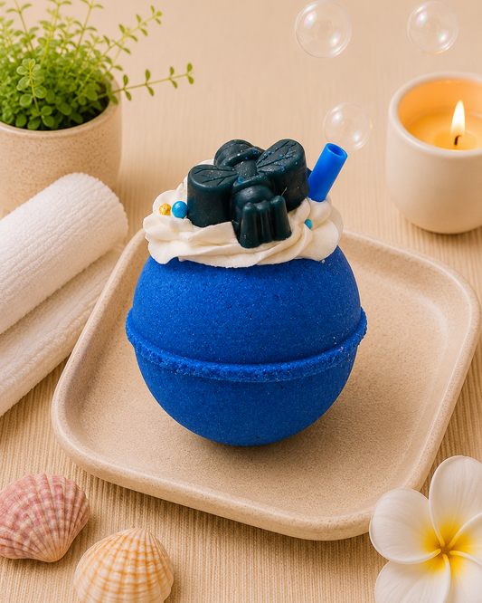 Blue bath bomb with black and white toppings on a beige tray with bubbles and a candle in the background.