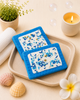 Two blue coasters with white centers and blue sprinkles on a beige tray, surrounded by decorative items.