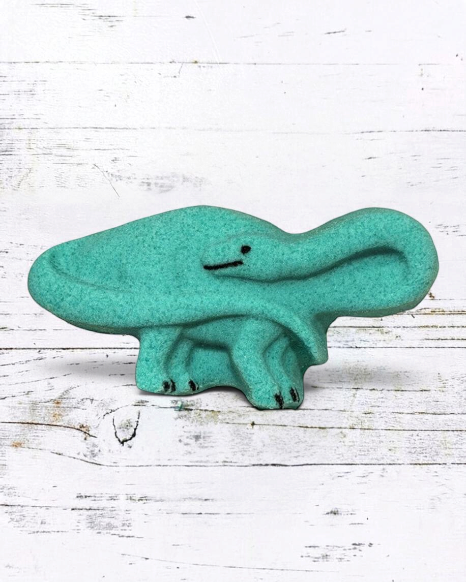 Calla Lily Cosmetics + CL kids teal brontosaurus shaped bath bomb with floral scent on a white wooden background