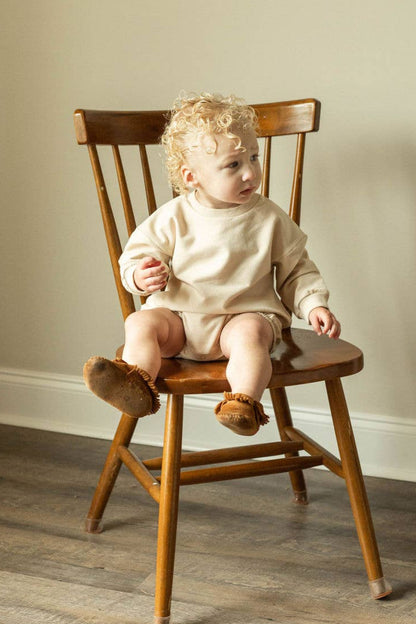 Child sitting on a wooden chair in a room with a neutral wall and a woven basket.