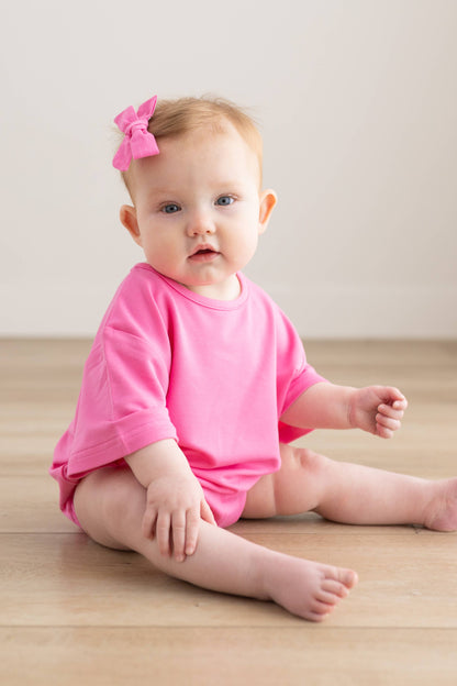 Baby in a pink outfit sitting on a wooden floor with a white background