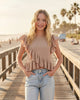 Girl wearing a beige textured asymmetrical ruffle top by Calla Lily Cosmetics + CL kids on a sunny beach boardwalk.