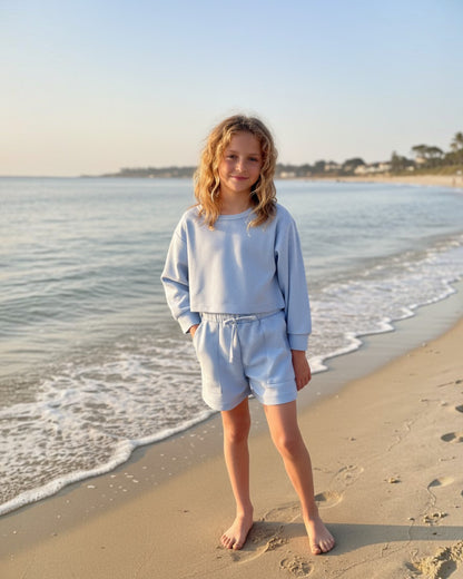 Girl wearing Calla Lily Cosmetics + CL kids baby blue waffle knit long sleeve shirt and shorts set on a beach.