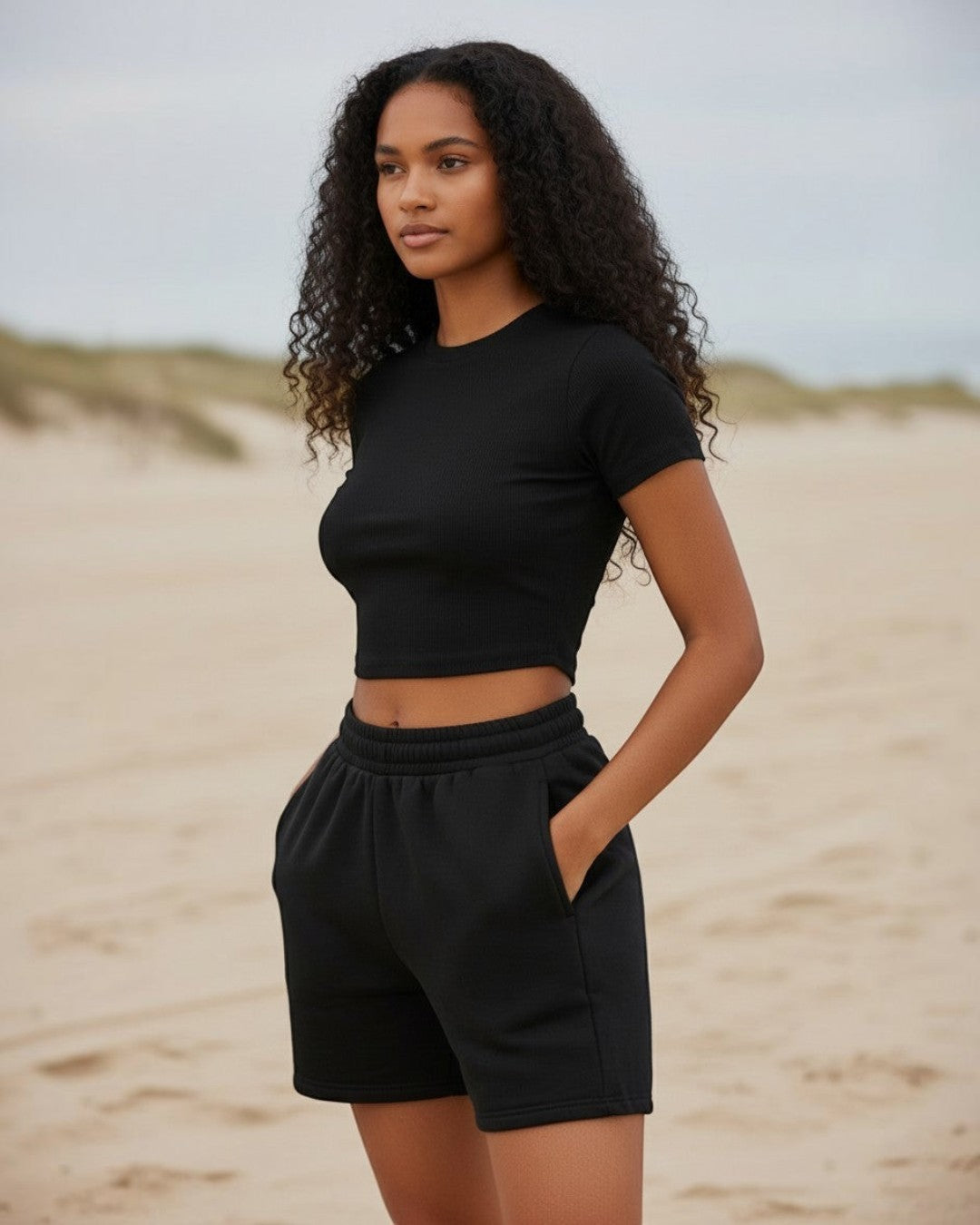 Model wearing Calla Lily Cosmetics + CL kids black ribbed crop tee and drawstring shorts on a sandy beach.