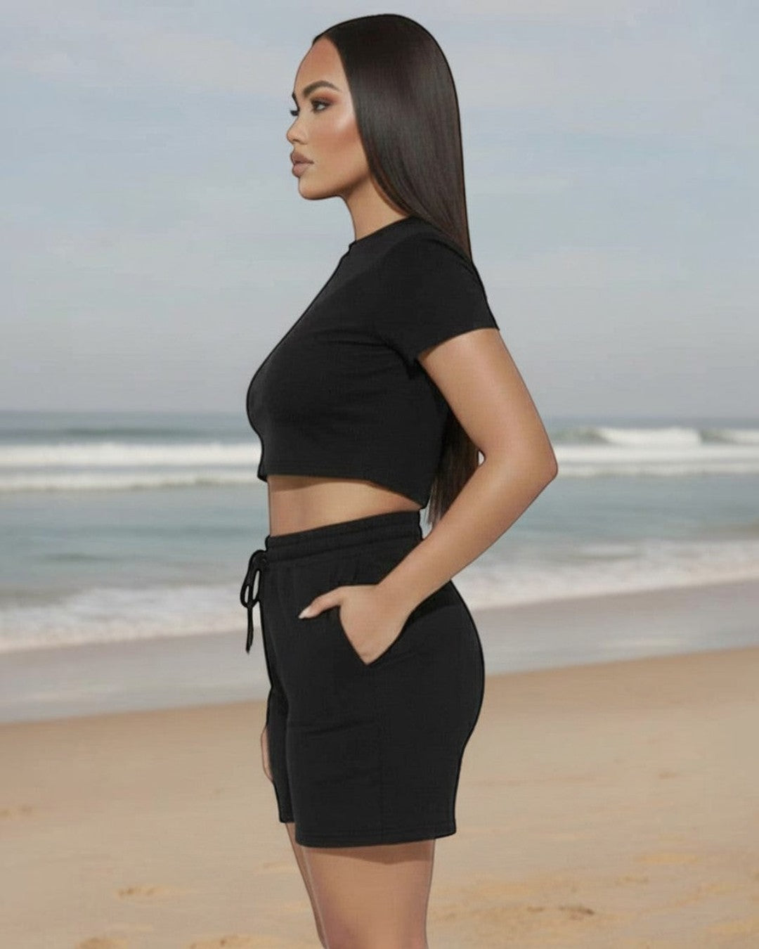 Model wearing Calla Lily Cosmetics + CL kids black two-piece set with fitted crop tee and drawstring shorts at beach.