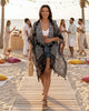 Calla Lily Cosmetics + CL kids black viscose kimono with mandala print and tassel hem worn by a woman on the beach.