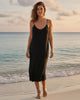 Woman wearing a black midi lounge dress with built-in bra by Calla Lily Cosmetics + CL kids on a beach at sunset.