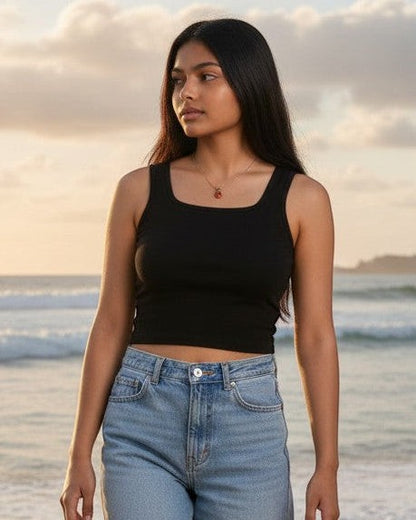 Model wearing a black Calla Lily Cosmetics + CL kids square neck crop tank with light wash jeans at the beach.