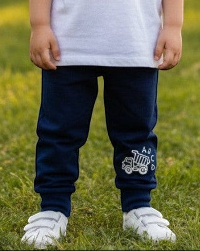Toddler wearing Calla Lily Cosmetics + CL kids blue cotton-blend joggers with a dump truck graphic in a park.
