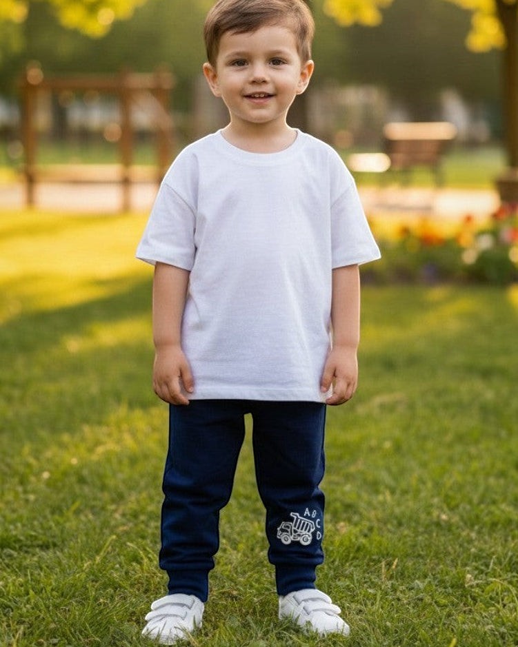 Toddler wearing Calla Lily Cosmetics + CL kids blue cotton-blend joggers with a dump truck graphic in a park.