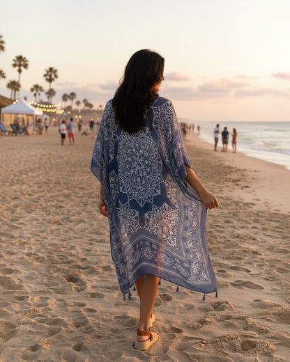 Woman wearing a blue viscose kimono cardigan with white mandala print and tassels on a beach at sunset by Calla Lily Cosmetics + CL kids