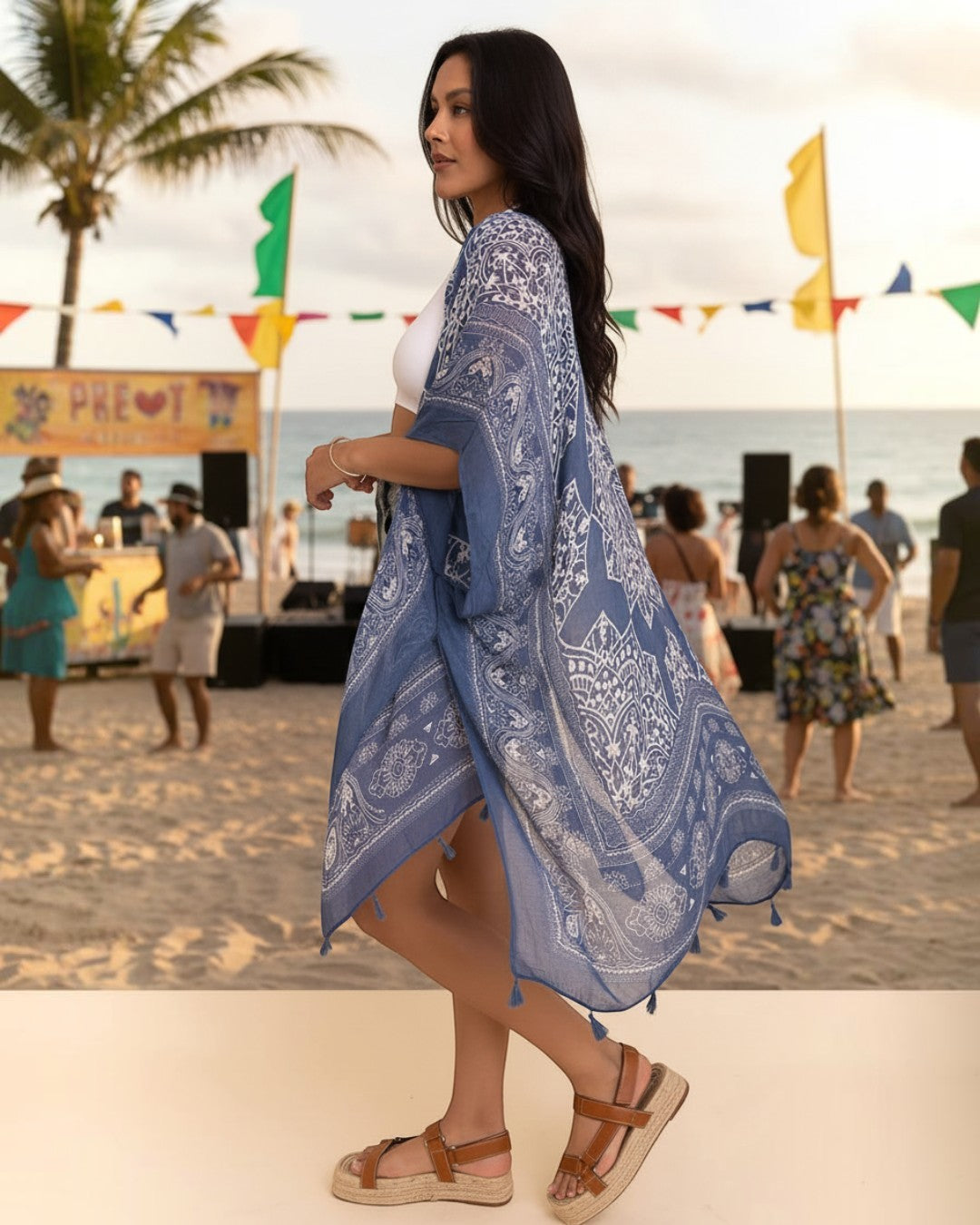 Woman wearing a blue viscose kimono cardigan with white paisley print and tassels at a beach festival by Calla Lily Cosmetics + CL kids