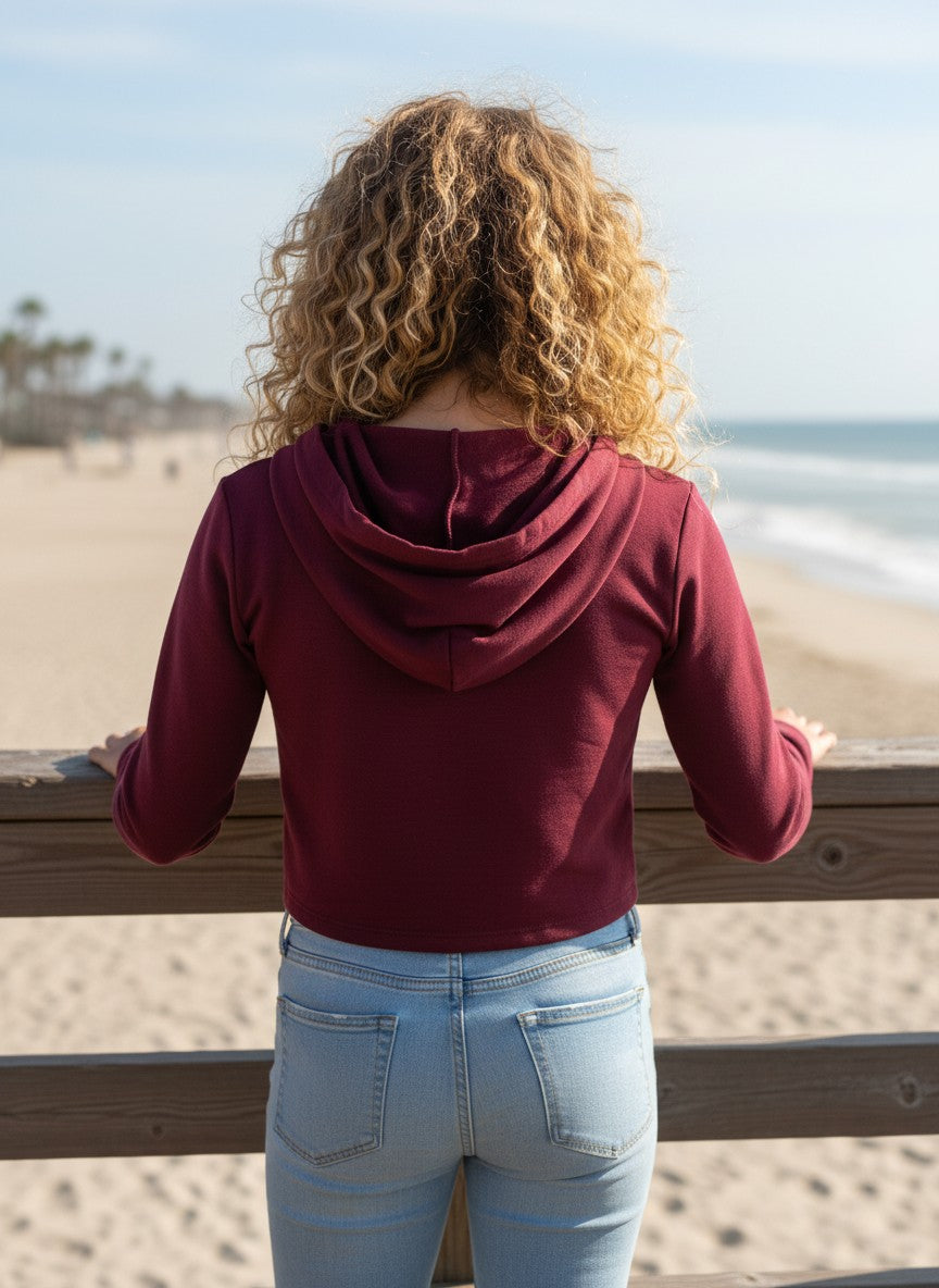 Model wearing a burgundy French Terry crop zip-up hoodie by Calla Lily Cosmetics + CL kids on a beach pier.