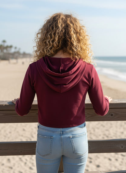 Model wearing a burgundy French Terry crop zip-up hoodie by Calla Lily Cosmetics + CL kids on a beach pier.