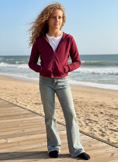 Calla Lily Cosmetics + CL kids burgundy French Terry crop zip-up hoodie worn by a girl on a beach boardwalk.