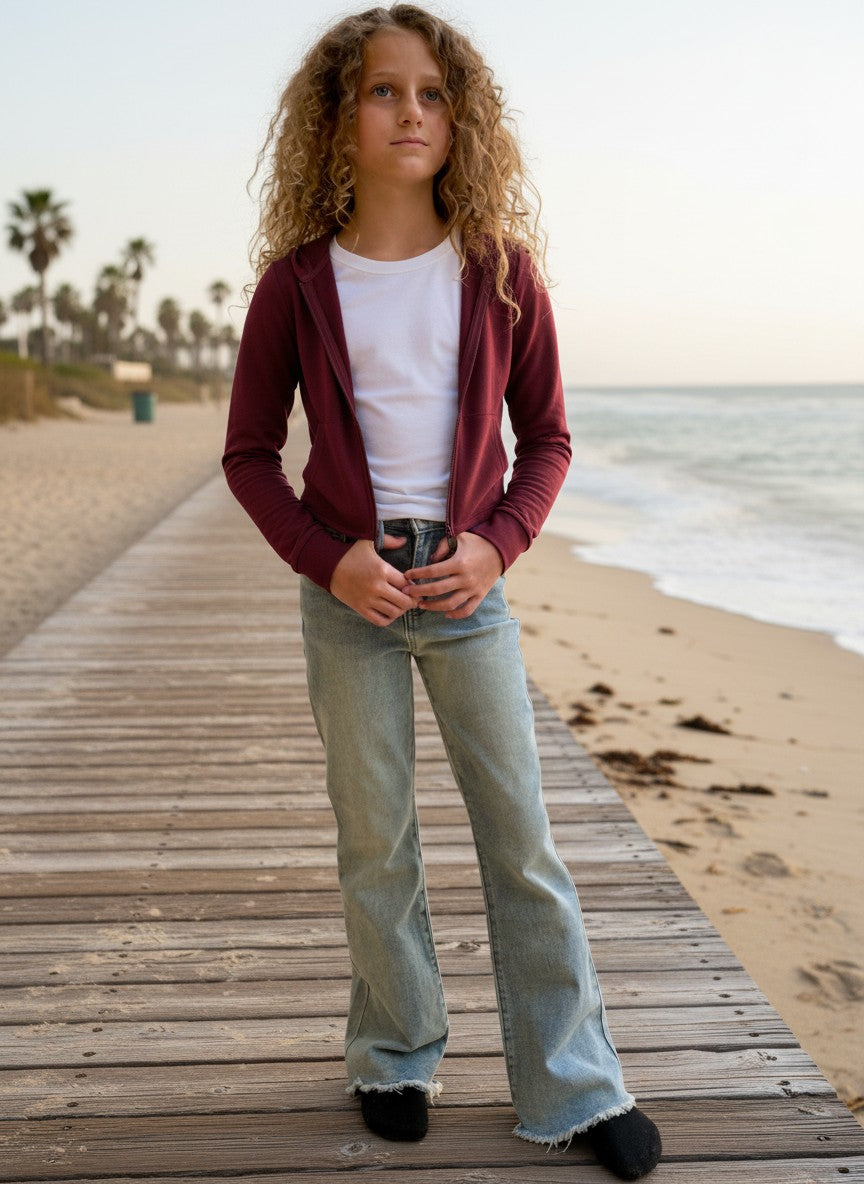 Model wearing a Calla Lily Cosmetics + CL kids burgundy French terry crop zip-up hoodie on a beach boardwalk.