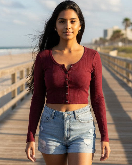 Model wearing a burgundy Calla Lily Cosmetics + CL kids ribbed long-sleeve button-up crop top on a beach boardwalk.