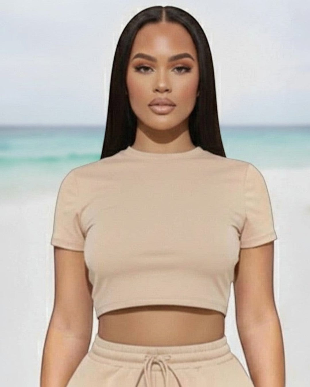 Model wearing Calla Lily Cosmetics + CL kids cream crop tee and drawstring shorts set on a beach background.
