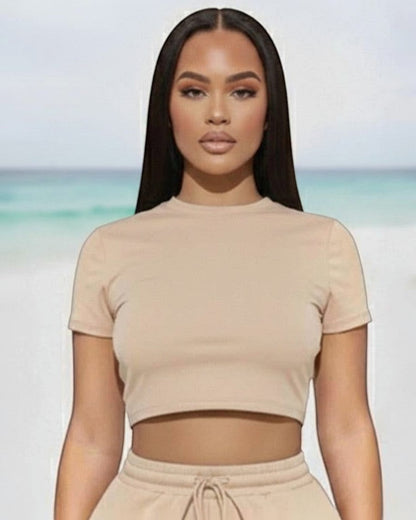 Model wearing Calla Lily Cosmetics + CL kids cream crop tee and drawstring shorts set on a beach background.
