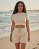 Model wearing Calla Lily Cosmetics + CL kids cream two-piece set with fitted crop tee and drawstring shorts on beach