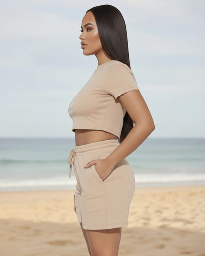 Model wearing Calla Lily Cosmetics + CL kids cream two-piece set with fitted crop tee and drawstring shorts on beach.