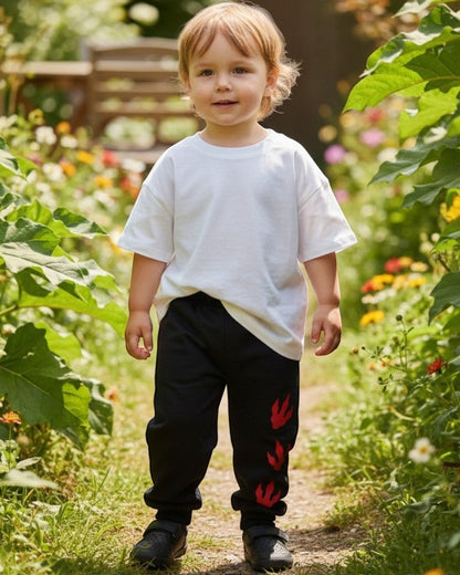 Toddler wearing Calla Lily Cosmetics + CL kids black cotton-blend joggers with red dragon paw print in a garden.
