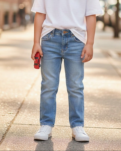 Young boy wearing Elevani Basic Fit blue denim jeans and a white t-shirt, standing on a city sidewalk.