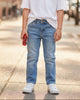Young boy wearing Elevani Basic Fit blue denim jeans and a white t-shirt, standing on a city sidewalk.