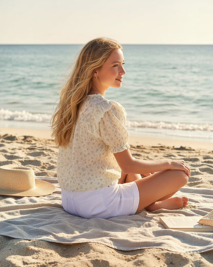 Girl wearing a Calla Lily Cosmetics + CL kids floral flowy top with ruffle sleeves while sitting on a beach blanket.