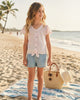 Girl wearing a Calla Lily Cosmetics + CL kids pink glitter flutter sleeve button-down shirt with denim shorts at beach