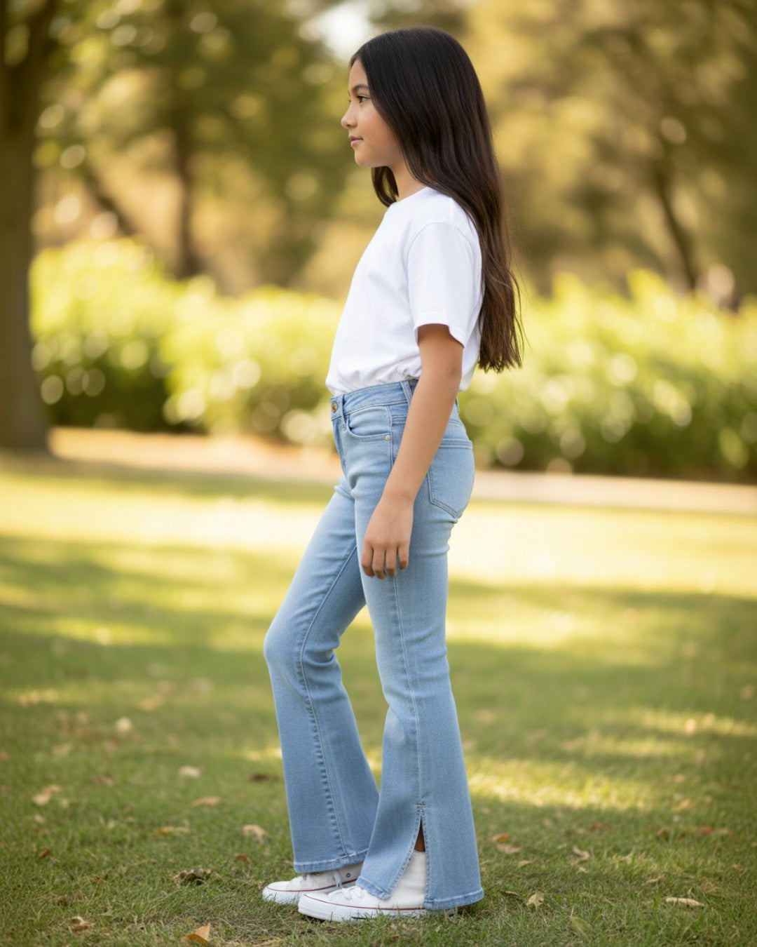 Girl wearing Calla Lily Cosmetics + CL kids light wash flare jeans with side slits and a white t-shirt in a park.