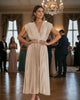 Woman wearing a Calla Lily Cosmetics + CL kids gold pleated maxi dress with a V-neck at a formal event.