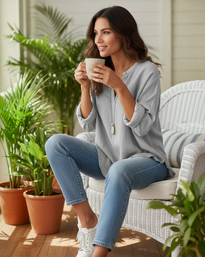 Woman wearing a grey long sleeve V-neck top by Calla Lily Cosmetics + CL kids, sitting in a chair with a coffee mug.