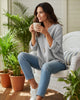 Woman wearing a grey long sleeve V-neck top by Calla Lily Cosmetics + CL kids, sitting in a chair with a coffee mug.