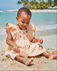 Baby girl wearing a Calla Lily Cosmetics + CL kids HoneyDrift dress with seashell embroidery on a sunny beach.