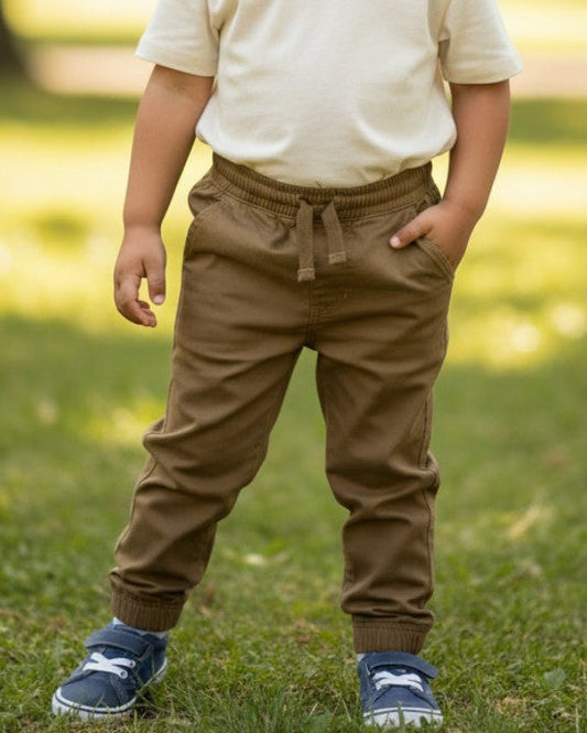 Toddler boy wearing Calla Lily Cosmetics + CL kids khaki drawstring pants in cotton blend standing in a park.